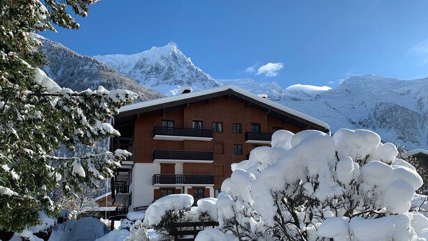 A wooden chalet with multiple balconies, surrounded by snow-covered trees and mountains. - Apartment with balcony, parking and pets allowed in Chamonix (Chamonix-Mont-Blanc)