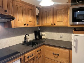 A kitchen with wooden cabinets, a black countertop, a coffee maker, and a microwave.