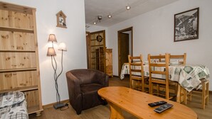 A cozy living room with a brown leather sofa, wooden dining table, and chairs. There is a lamp, a wooden cabinet, and a framed picture on the wall. - Apartment with balcony, parking and pets allowed in Chamonix (Chamonix-Mont-Blanc)