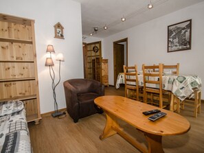A cozy living room with a brown leather sofa, wooden dining table, and chairs. There is a lamp, a wooden cabinet, and a framed picture on the wall. - Apartment with balcony, parking and pets allowed in Chamonix (Chamonix-Mont-Blanc)