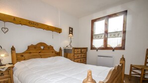 A wooden bed with a heart-shaped headboard, a wooden dresser, a nightstand with a lamp, and a window with a heart-patterned curtain. - Apartment with balcony, parking and pets allowed in Chamonix (Chamonix-Mont-Blanc)