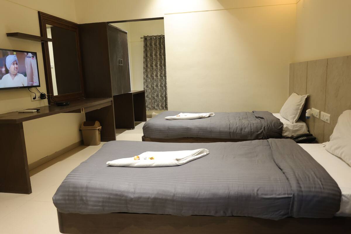 A hotel room with two beds, a TV, a desk, and a mirror.