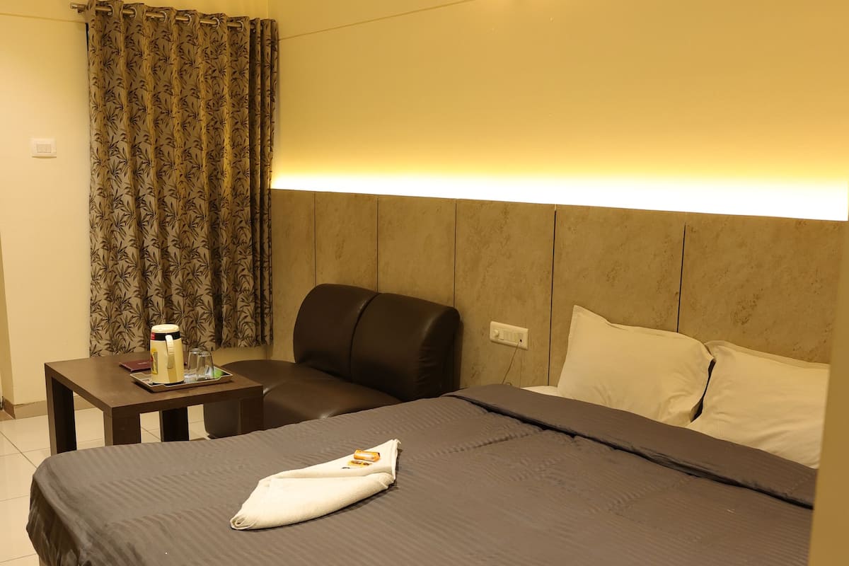 A hotel room with a bed, a bedside table, a chair, a lamp, and a curtain.