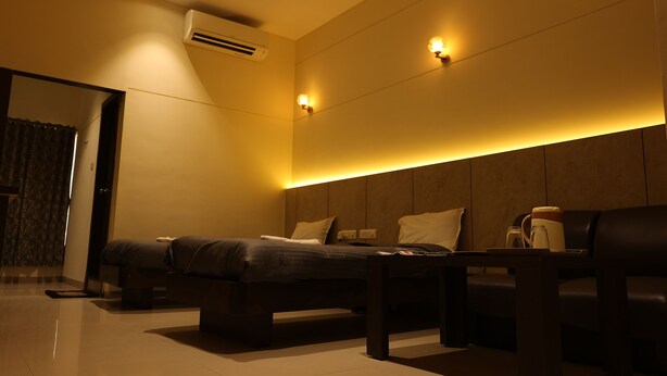 A modern hotel room with a bed, a sofa, a coffee table, and a wall-mounted air conditioner. - Hotel Galaxy Deluxe (Jalna)