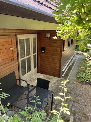 A wooden cabin with a glass door, a small patio with a table and chairs, and a number 39 sign on the wall.