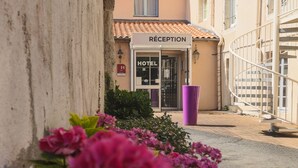 A hotel reception with a sign, a staircase, and a purple trash bin. - Hôtel Le Cheval Blanc (Saint-Maixent-l'Ecole)