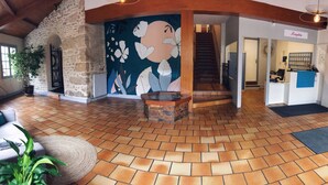 A spacious lobby with a stone wall, a large floral mural, a staircase, and a reception desk. - Hôtel Le Cheval Blanc (Saint-Maixent-l'Ecole)