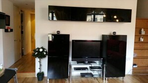 Ein Wohnzimmer mit Flachbildfernseher auf einem Schrank, einer Topfpflanze und Holzboden.