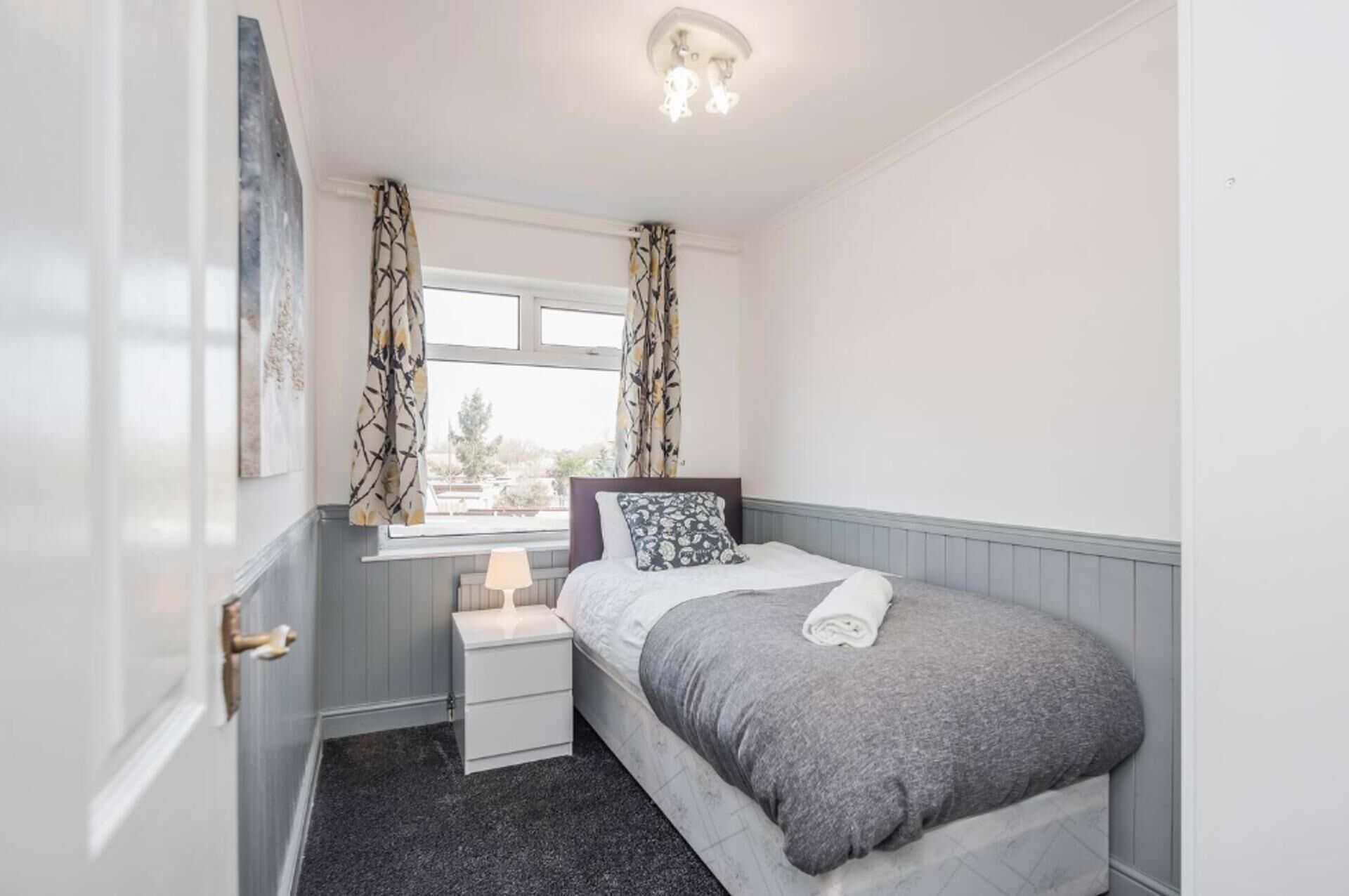 A bedroom with a bed, a nightstand, a lamp, and a window with curtains.