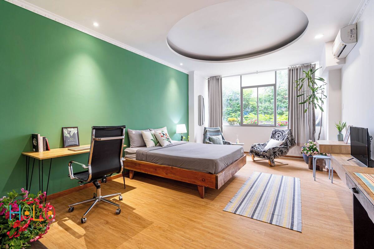 A modern bedroom with a bed, desk, chair, and a large window.