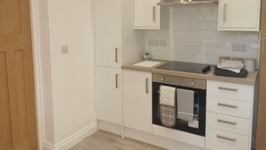 Una cocina moderna con armarios blancos, una campana extractora de acero inoxidable, horno empotrado y una puerta de madera.