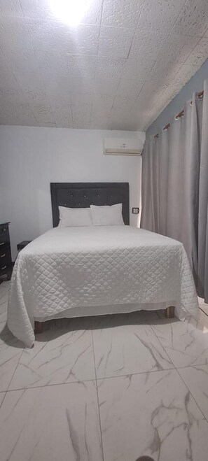 A bedroom with a bed, a dresser, and an air conditioning unit on the wall. - Inviting 1-bed Apartment in Ocho Rios (Ocho Rios)