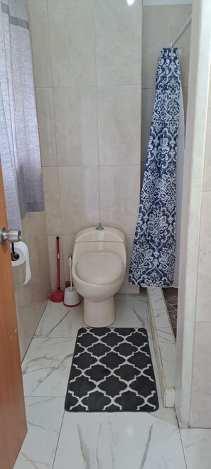A bathroom with a toilet, a blue patterned shower curtain, a white floor mat, and a red broom. - Inviting 1-bed Apartment in Ocho Rios (Ocho Rios)