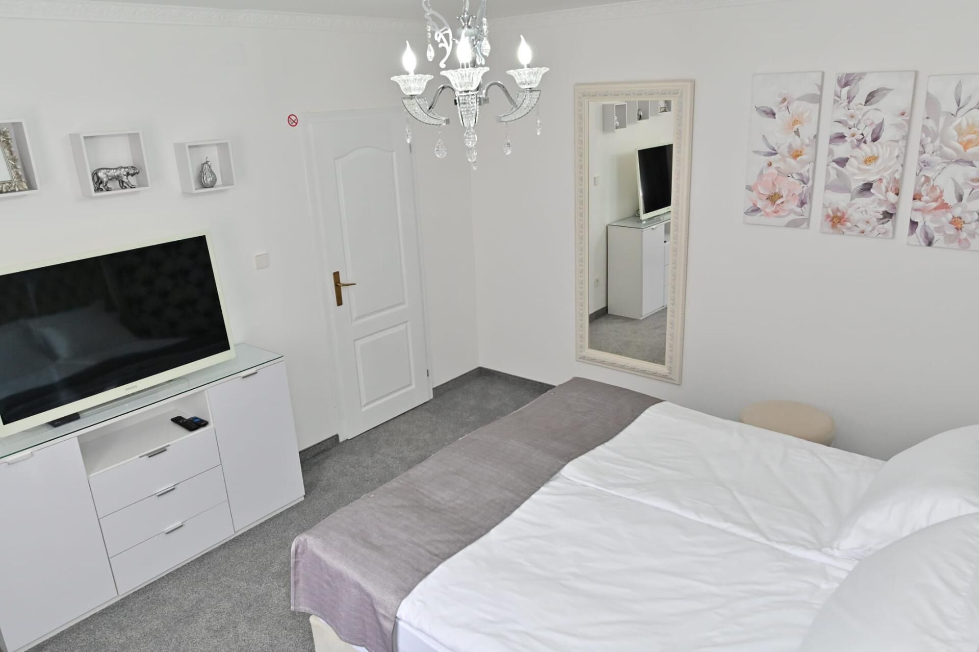 A bedroom with a bed, a TV on a stand, a dresser, a mirror, and wall art.