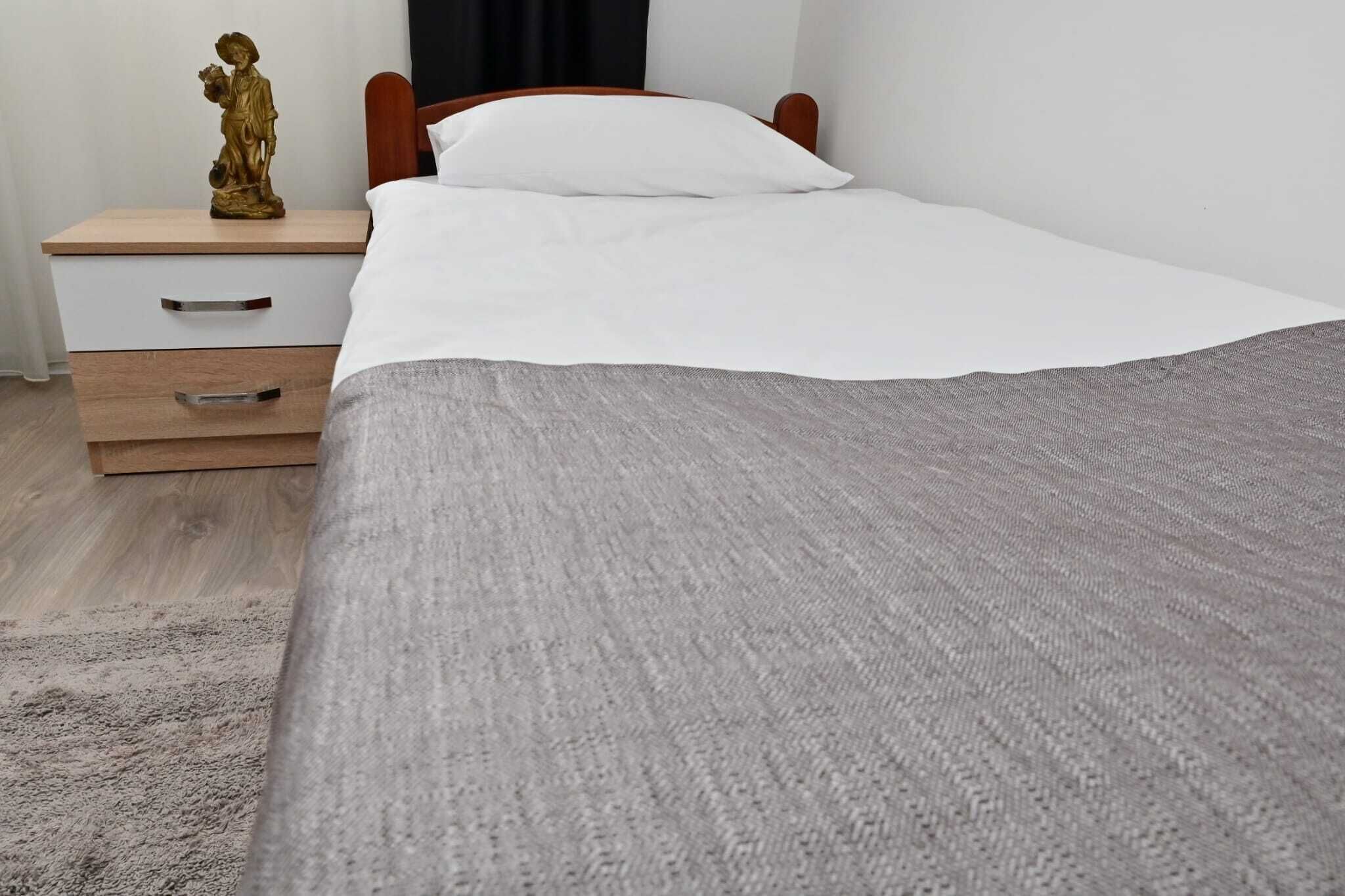 A neatly made bed with a grey blanket, a wooden nightstand with a drawer, and a small golden statue on the nightstand.
