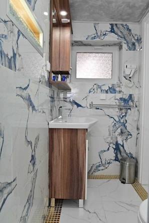 A bathroom with marble walls, a wooden vanity, a sink, a mirror, and a window.