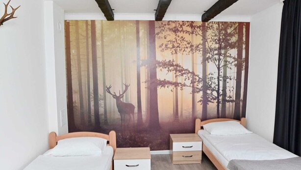 A bedroom with two single beds, a large forest mural on the wall, and a modern ceiling design.