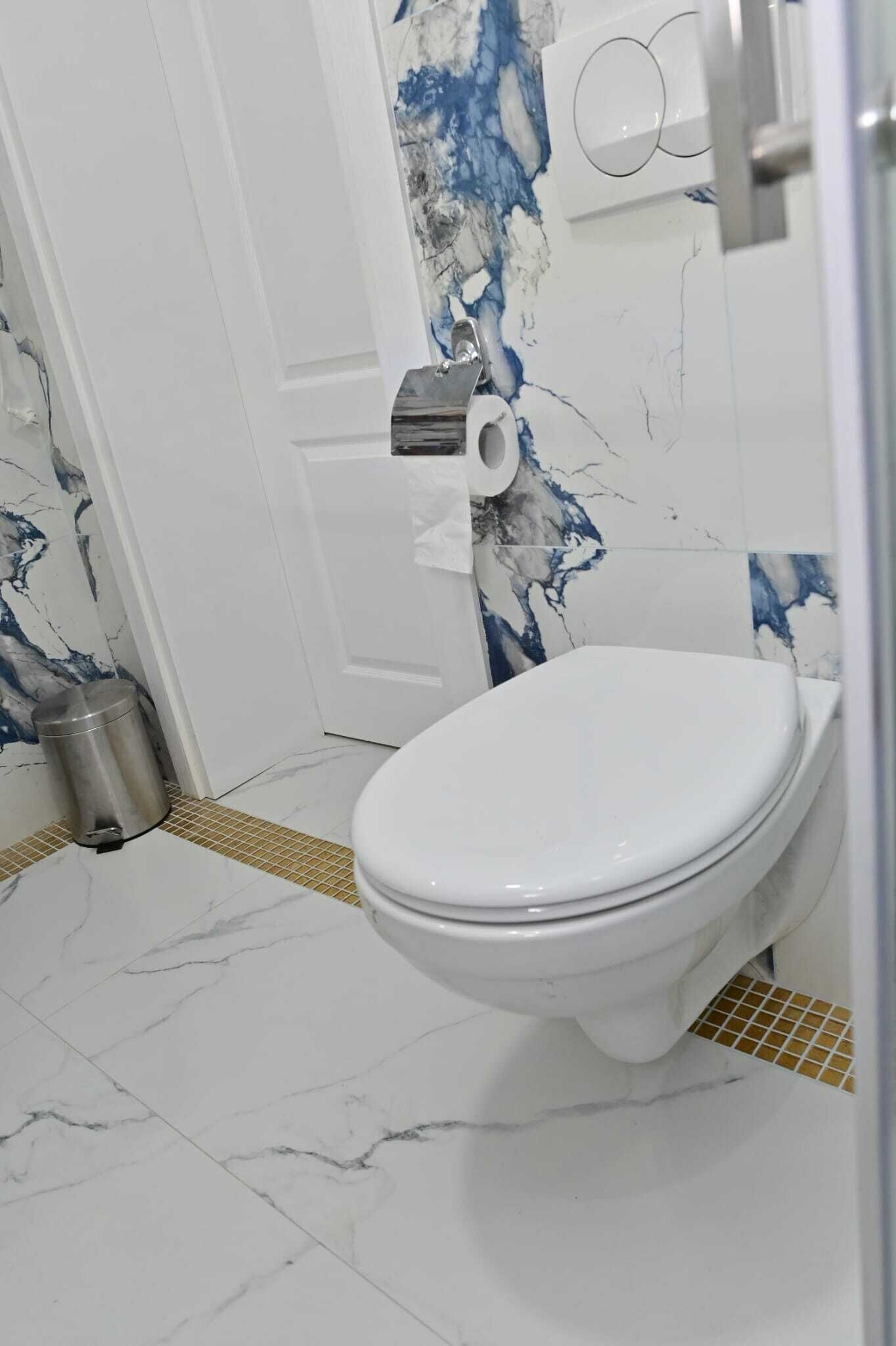 Een badkamer met een wit toilet, wanden met een marmerlook en een betegelde vloer.