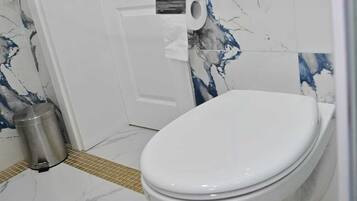 A bathroom with a white toilet, marble-patterned walls, and a tiled floor.
