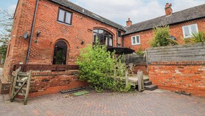 A red brick house with a small garden, a wooden gate, and a paved driveway.