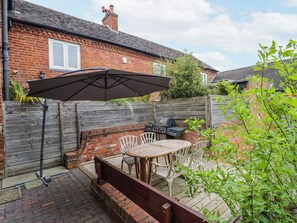 A patio with a table and chairs, a grill, and a wooden fence. - The Haybarn (Lichfield)