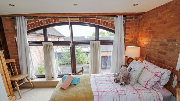 A bedroom with a large arched window, a bed with multiple pillows, a chair, and a lamp.