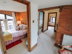A bedroom with a bed, a red rug, a wooden chair, and a mirror. - The Haybarn (Lichfield)
