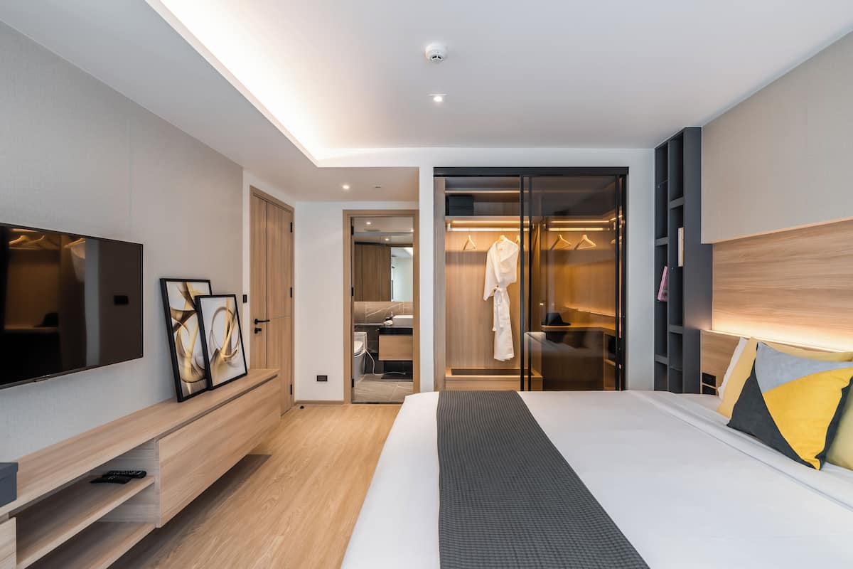 Quarto de hotel moderno com uma cama grande, televisão de tela plana, mesa de cabeceira e um closet espaçoso com espelho.