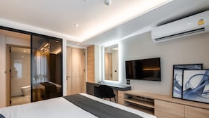 A modern hotel room with a large bed, a desk with a chair, a flat-screen TV, and an air conditioning unit.