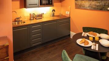 A compact kitchen with a microwave, toaster, and sink. There is a dining table with plates, glasses, and a croissant.