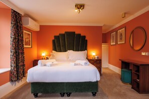 Una cama bien hecha con sábanas blancas, un cabecero tapizado en verde y dos lámparas de noche.