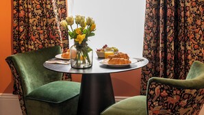 A dining area with two green upholstered chairs, a round table, and a vase with yellow flowers. - The Fanny Talbot  (Barmouth)