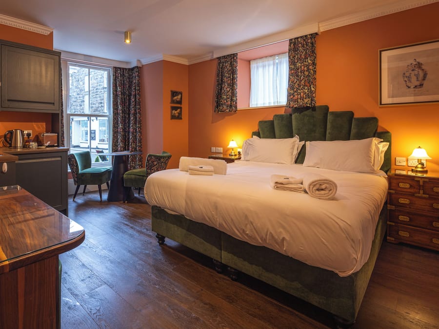 A hotel room with a bed, a desk, a chair, a dresser, and a window with curtains.
