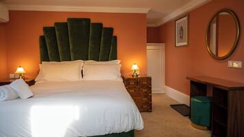 A neatly made bed with white linens, two bedside lamps, a green upholstered headboard, a wooden nightstand with drawers, a green waste bin, and a mirror on the wall.