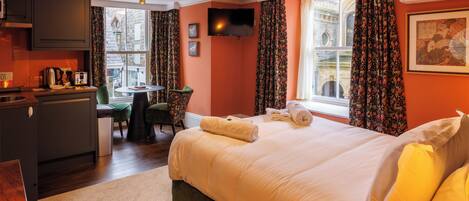 Habitación de hotel con cama, escritorio, silla, televisor y ventana con cortinas.