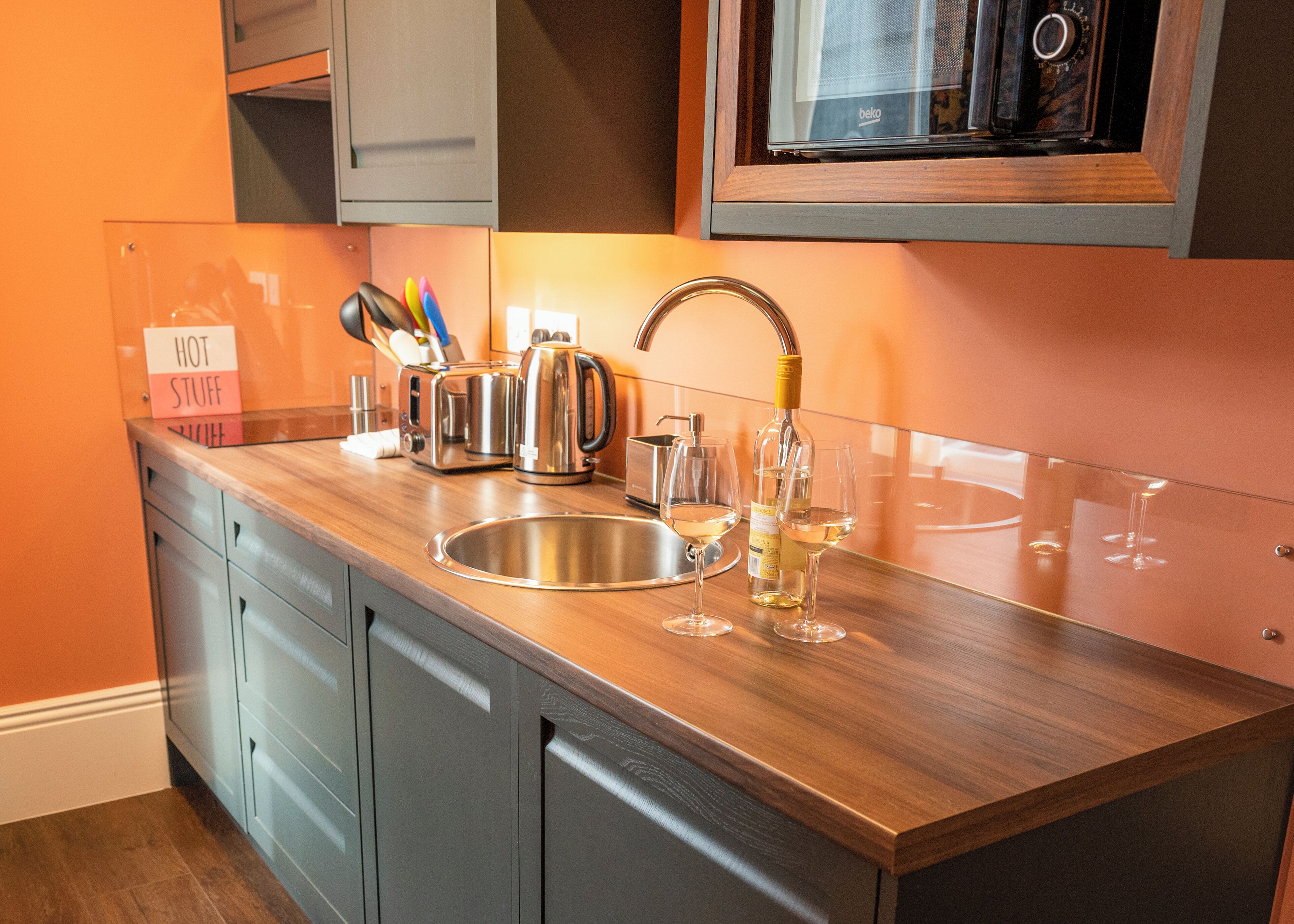 A kitchen with a stainless steel sink, a toaster, a kettle, and a wine bottle.