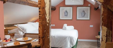 A cozy room with a bed, a dining table with breakfast, and two framed artworks on the wall.