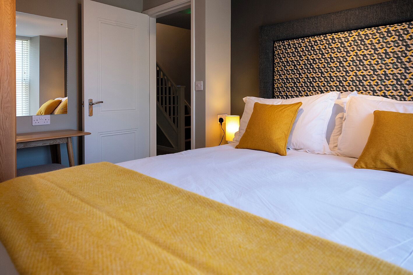 A hotel room with a bed, a bedside table, a mirror, and a patterned headboard.