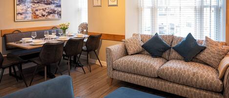 A modern living room with a sofa, two armchairs, a dining table set with plates and glasses, and a painting on the wall.