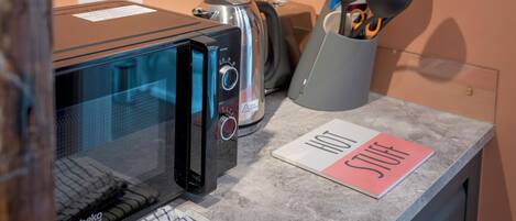 A kitchenette with a microwave, toaster, and a utensil holder on the counter.