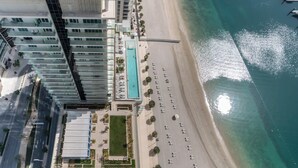 Vista aérea de um hotel à beira-mar com piscina, cadeiras de praia e um porto de iates.