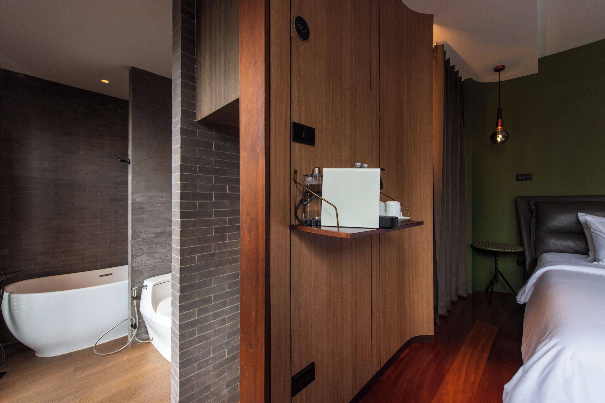 A modern bathroom with a freestanding bathtub, a wooden vanity, and a bedside table with a lamp.