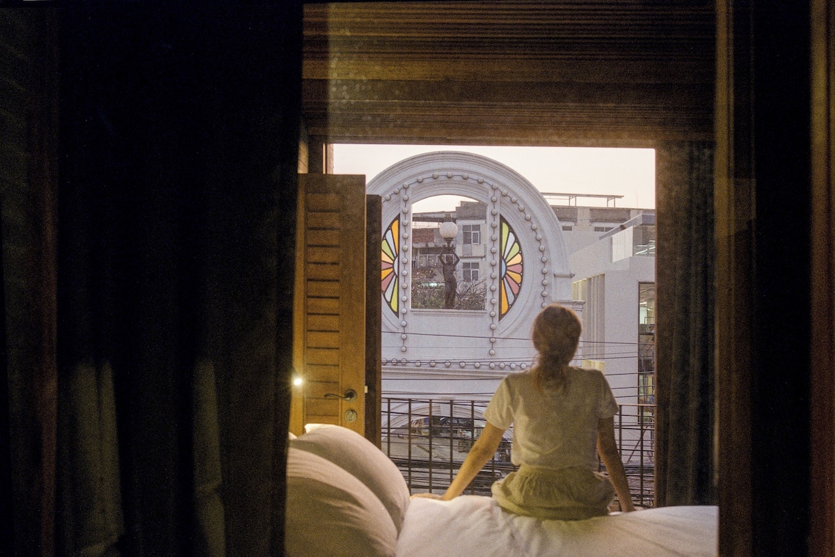 A room with a large window, a bed, and a view of a building with a circular stained glass window.