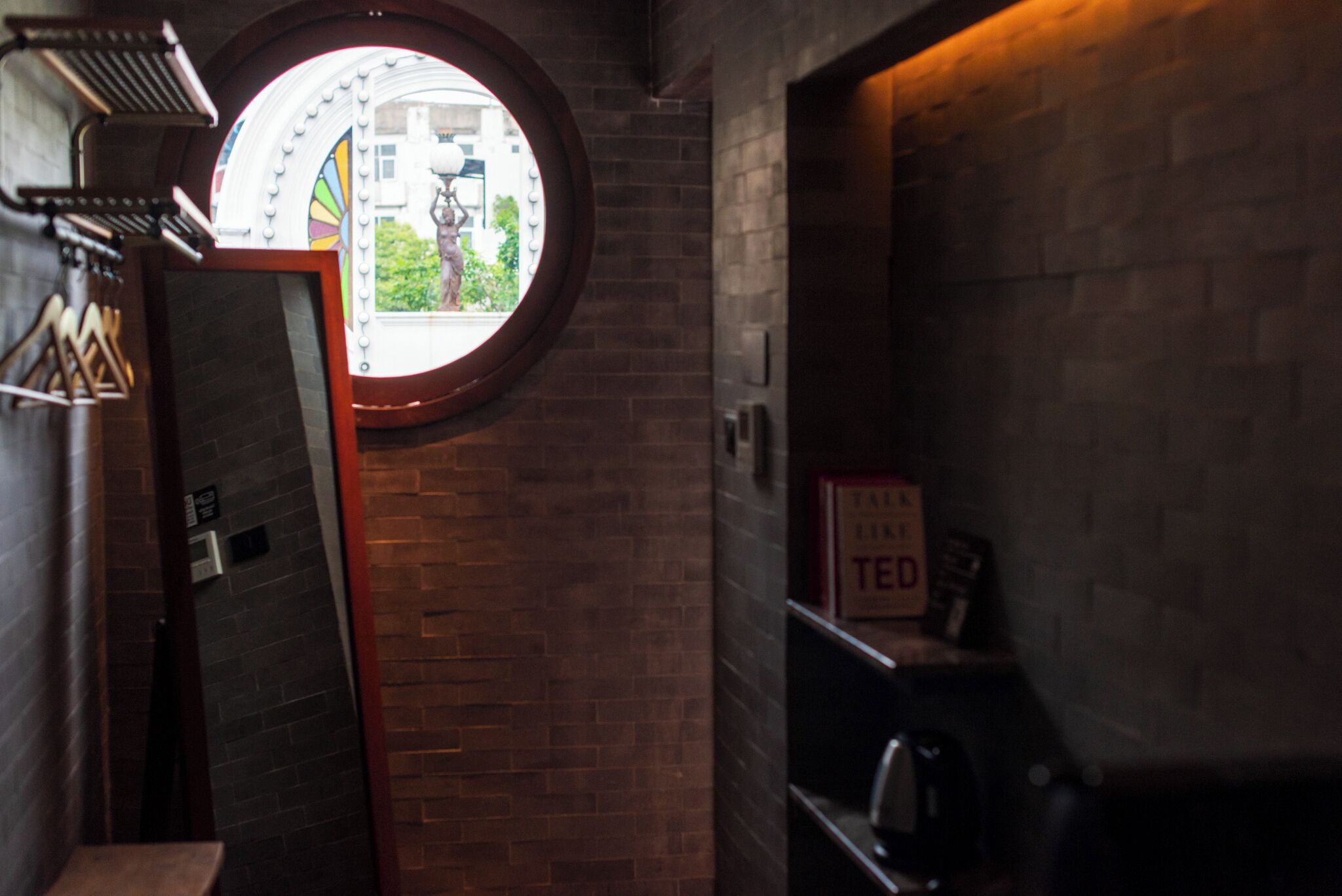 A narrow corridor with a circular window, brick walls, and a shelf with a sign that reads "TED".