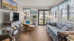 Een woonkamer met een televisie, rieten meubels, een bank en uitzicht op een balkon.