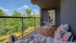 A balcony with a wooden floor, white and striped cushions, and a white chair.