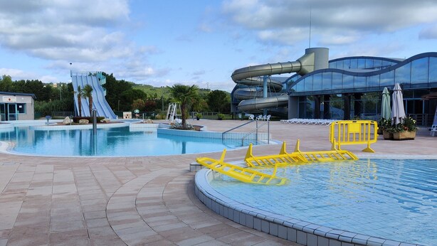 Zona de piscina con tobogán y un edificio moderno con amplios ventanales.