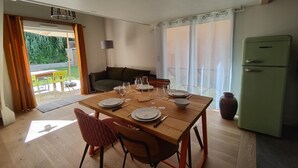 Un comedor con una mesa de madera dispuesta para cuatro personas, un refrigerador verde y un sofá al fondo.