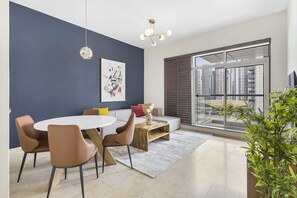 Ein modernes Wohnzimmer mit einem runden Esstisch, braunen Stühlen, einem weißen Sofa und einem großen Fenster mit Blick auf hohe Gebäude.