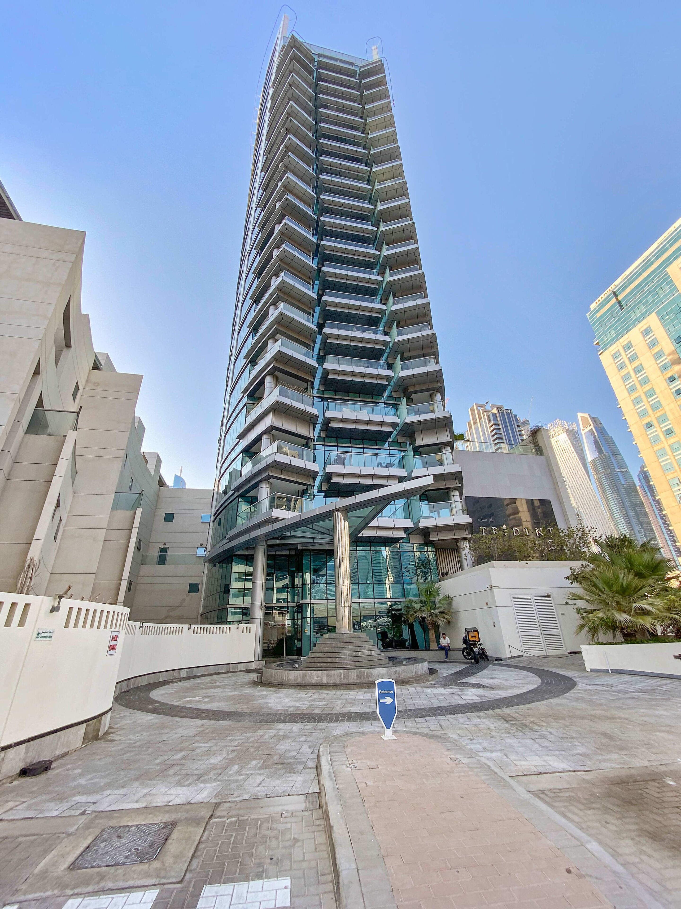 A tall, modern building with a unique angular design, featuring multiple balconies and a glass facade.